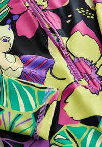 Barevná látka s květinovým vzorem v růžové, zelené a žluté barvě s texturovaným povrchem. Obsahuje růžový zip a kontrastní šití.