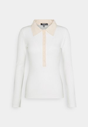Polo à manches longues en tissu blanc côtelé avec un col et une patte de boutonnage contrastants beige. Dispose de six boutons et d'une coupe ajustée.