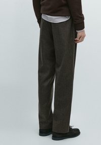 Pantaloni di lana marrone con texture, a vestibilità morbida, con gambe larghe e un motivo sottile, abbinati a scarpe di camoscio nere.