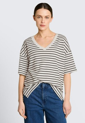 Femme portant un haut blanc ample à manches courtes et col en V avec des rayures horizontales noires, rentré dans un jean bleu taille haute.