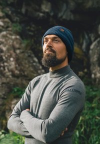 Maglia grigia a maniche lunghe con collo alto, caratterizzata da una texture sottile e un logo blu sulla manica, abbinata a un cappellino a costine blu navy.