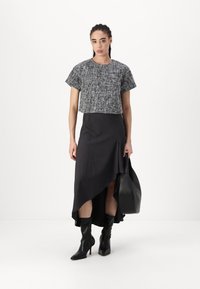 Top corto in bianco e nero con texture abbinato a una gonna asimmetrica grigio scuro, stivali neri sopra il ginocchio e una grande borsa nera.