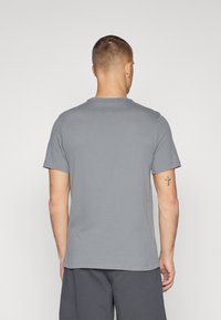 Camiseta de algodón gris con cuello redondo y mangas cortas; exhibida desde la parte de atrás, mostrando una textura suave y sin patrones visibles.