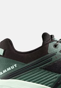 Svart och grön atletisk sko med en texturerad ovandel, strömlinjeformad design, förstärkt sula och kontrasterande ljusgröna accenter.