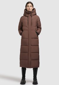 Rudas paminkštas ilgas paltas su auk�šta apykakle, su užtrauktuku, šoninėmis kišenėmis ir juodais akcentais. Dėvimas su juodais kariniais batais.