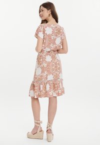 Vestido de patrón paisley floral en blanco con tonos rosas y naranjas. Presenta mangas cortas, dobladillo con volantes y una cintura ajustada, combinado con sandalias de cuña beige.