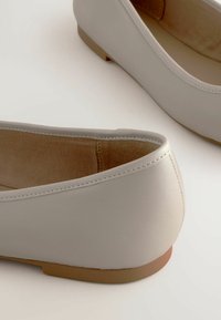 Valkeat nahkakengät, joissa on pyöreä varvasosa ja matala, vaaleanruskea korko. Sisäpuolella pehmeä vaaleanbeige kangasvuori ja hienostunut ompeluyksityiskohta.