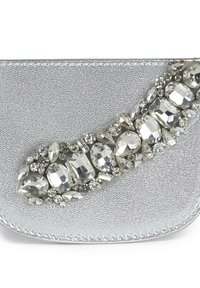 Clutch sintetico argento con finitura texturizzata, caratterizzato da un insieme di accenti chiari e metallici in varie forme e dimensioni lungo un lato.
