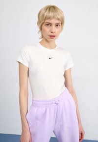 Bílý přiléhavý tričko s krátkými rukávy a černým logem Nike na hrudi, doplněné fialovými tepláky na šňůrku.