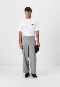Tricou alb cu mânecă scurtă și un logo negru pe buzunar, asortat cu pantaloni gri cu dungi, cu talie înaltă și adidași negri. Poartă o geantă neagră.