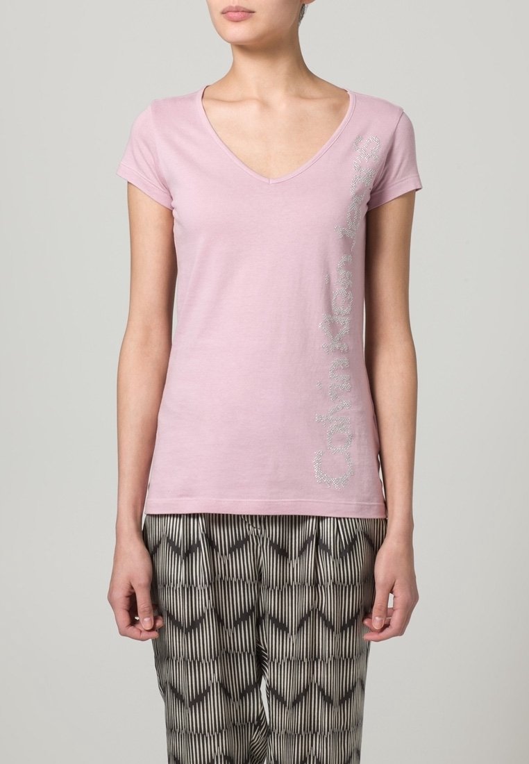 Camiseta de algodón rosa con escote en V y mangas cortas, con texto brillante en el lateral. Combinada con pantalones estampados en blanco y negro.