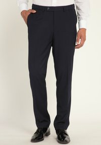 Pantaloni navy dal taglio sartoriale, realizzati in un tessuto liscio con parte anteriore piatta e tasche, abbinati a scarpe eleganti nere lucide.