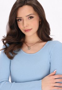 Top a maniche lunghe ribbed di colore azzurro chiaro con scollatura rotonda, abbinato a una collana in tono oro con pendente a spirale. Tessuto morbido.