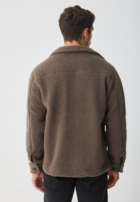 Bruine fleece jas met een gestructureerd oppervlak, een grote kraag en knoopmanchetten. De achterkant heeft een relaxte pasvorm en een ronde zoom.