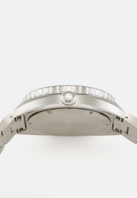 Orologio in acciaio inox con cassa rotonda, lunetta testurizzata e cinturino semplice. Presenta un logo sulla corona e un retro liscio e privo di marchi.