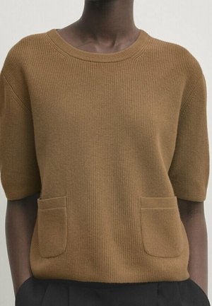 Pull en maille marron à manches courtes avec un col rond et deux poches avant, porté avec un pantalon noir.