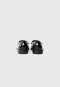 Sorte patentlæder loafers med glat tekstur, rundt sølvhardwaredetalje ved hælen og en slank silhuet.