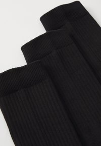 Sorte ribbede sokker med et struktureret stof og elastiske manchetter. Tre par er arrangeret side om side, hvilket viser et ensartet design.