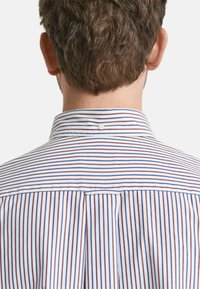 Chemise à rayures avec des lignes étroites bleues et bordeaux sur un tissu blanc. Comprend une fermeture à bouton à l'arrière du col.