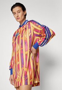 Colorful oversized jersey dress featuring a floral pattern, with vertical stripes in pink and yellow, blue collar, and long sleeves.