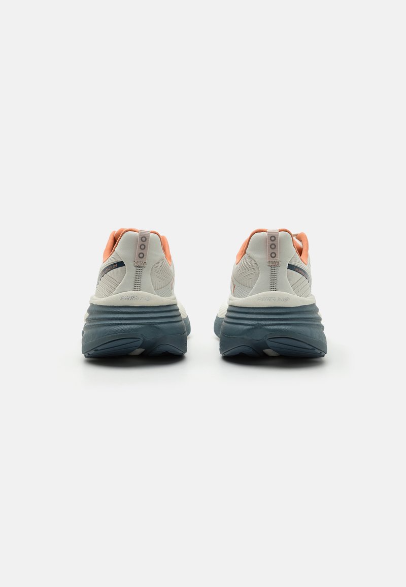 Baskets de course blanches et orange avec un dessus texturé, semelle rembourrée bleu marine et un design de talon prononcé. Présente une étiquette de marque sur le talon.