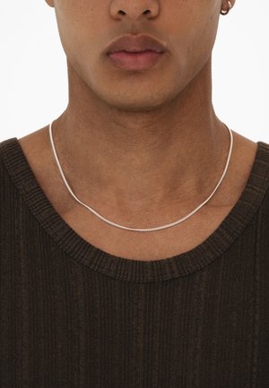 Silver chain necklace worn over a dark ribbed shirt, featuring a smooth, streamlined design with a subtle sheen.