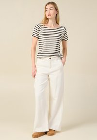 Top de rayas, de manga corta en crema y azul marino; combinado con pantalones blancos de pierna ancha y cintura alta; zapatos marrones tipo slip-on.