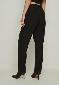 Black tailored trousers with a straight cut, featuring two back pockets and a smooth texture. Paired with black heeled shoes.