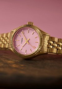 Reloj en tono dorado con bisel acanalado, esfera rosa y marcadores de horas dorados. Terminado con una pulsera de metal enlazada para aportar textura y durabilidad.