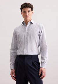 Camicia con maniche lunghe e bottoni di colore azzurro chiaro con un piccolo motivo floreale multicolore; tessuto morbido; design colletto; abbinata a pantaloni scuri.