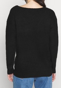 Svart oversized stickad tröja med vid halsringning och sänkta axelsömmar. Texturen är mjuk och passformen är avslappnad, vilket passar bra med blå jeans.