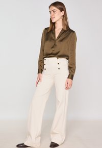 Blusa di seta verde oliva con scollo a V profondo e maniche lunghe, abbinata a pantaloni a gamba larga color crema a vita alta con dettagli in bottone dorato.