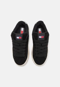 Czarne zamszowe sneakersy z białą gumową podeszwą, sznurówkami i metką marki z czerwono-białymi oraz niebieskimi akcentami na języku.