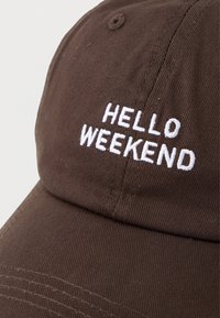 Casquette de baseball en tissu brun avec un texte brodé blanc disant "HELLO WEEKEND" sur le panneau avant.