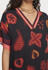 Top in tessuto nero con scollatura a V e maniche corte. Presenta audaci motivi floreali rossi e arancioni. Decorato con dettagli rosa sul colletto.