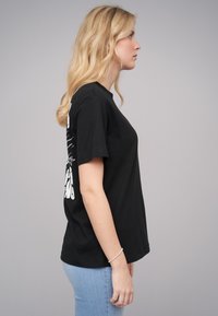Black cotton t-shirt with short sleeves, featuring white graphic print on the left side. Casual fit, shown on a person in profile.