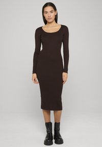 Robe marron côtelée à manches longues, col en U, silhouette ajustée et longueur mi-mollet, associée à des bottines noires.