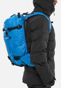 Sac à dos bleu avec plusieurs compartiments, fabriqué en tissu durable. Comprend des bretelles noires, des boucles et un design épuré et structuré.