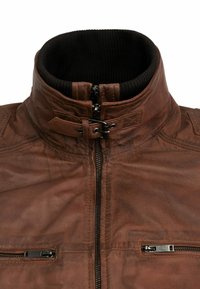 Chaqueta de cuero marrón con cuello alto, forro interior negro, cremallera frontal, hebilla en el cuello y bolsillos en el pecho con cremallera horizontal.