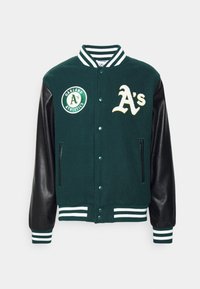 Veste universitaire en laine verte avec manches en cuir noir. Présente un écusson logo Oakland Athletics blanc et vert, une fermeture à boutons et des poignets rayés.