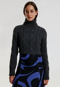 Kariertes, dunkelgraues Strickpullover mit hohem Rollkragen und langen Ärmeln, kombiniert mit einem schwarzen Kleid mit blauen wirbelnden Mustern.