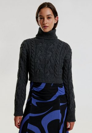 Kariertes, dunkelgraues Strickpullover mit hohem Rollkragen und langen Ärmeln, kombiniert mit einem schwarzen Kleid mit blauen wirbelnden Mustern.