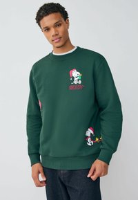 Zöld pulóver, amelyen Snoopy tervezés látható mikulás sapkában, bordás mandzsettákkal és szegéllyel. Puha anyagból készült, hímzett részletekkel.