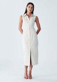 Mouwloze beige midi-jurk met knoopsluiting aan de voorkant, een kraag en een voorsplit. Gemaakt van een lichtgewicht stof met een gladde textuur.