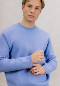 Lyseblå genser med rund hals laget av mykt strikket materiale, med ribbestrikkede mansjetter. Designet har en avslappet passform og sømløse skuldre.