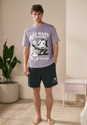 Light purple cotton t-shirt with graphic print; black shorts with cartoon cat design; indoor setting with plants and neutral colors.