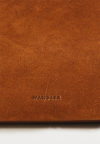 Pieskový semišový materiál s jemnou Textúrou, s embosovaným značkovaním "WANDLER". Dizajn je jednoduchý, bez ďalších vzorov alebo kovových detailov.