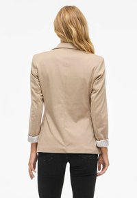 Beige blazer met gestructureerde schouders en lange mouwen. Opgerolde manchetten onthullen een gestreepte voering en hebben een gestroomlijnde, op maat gemaakte pasvorm.