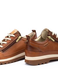 Chaussures en cuir marron au design arrondi, avec une fermeture éclair sur le côté et des lacets texturés. Semelle en caoutchouc épaisse et détails de marque discrets.