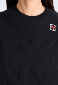 Felpa nera con motivo in rilievo del logo "DKNY", colletto a costine e piccolo logo ricamato in rosso, bianco e nero sul petto.